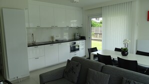 A modern kitchen with white cabinets and a dining area with a grey sofa and a table. - Relaxing Escape in Knokke (Knokke-Heist)