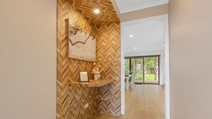 Un couloir avec un mur en bois à motifs en chevrons, un tableau encadré et une petite étagère ornée de fleurs.