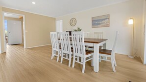 Un coin repas avec une table en bois et des chaises blanches, une horloge, un tableau et un lampadaire.