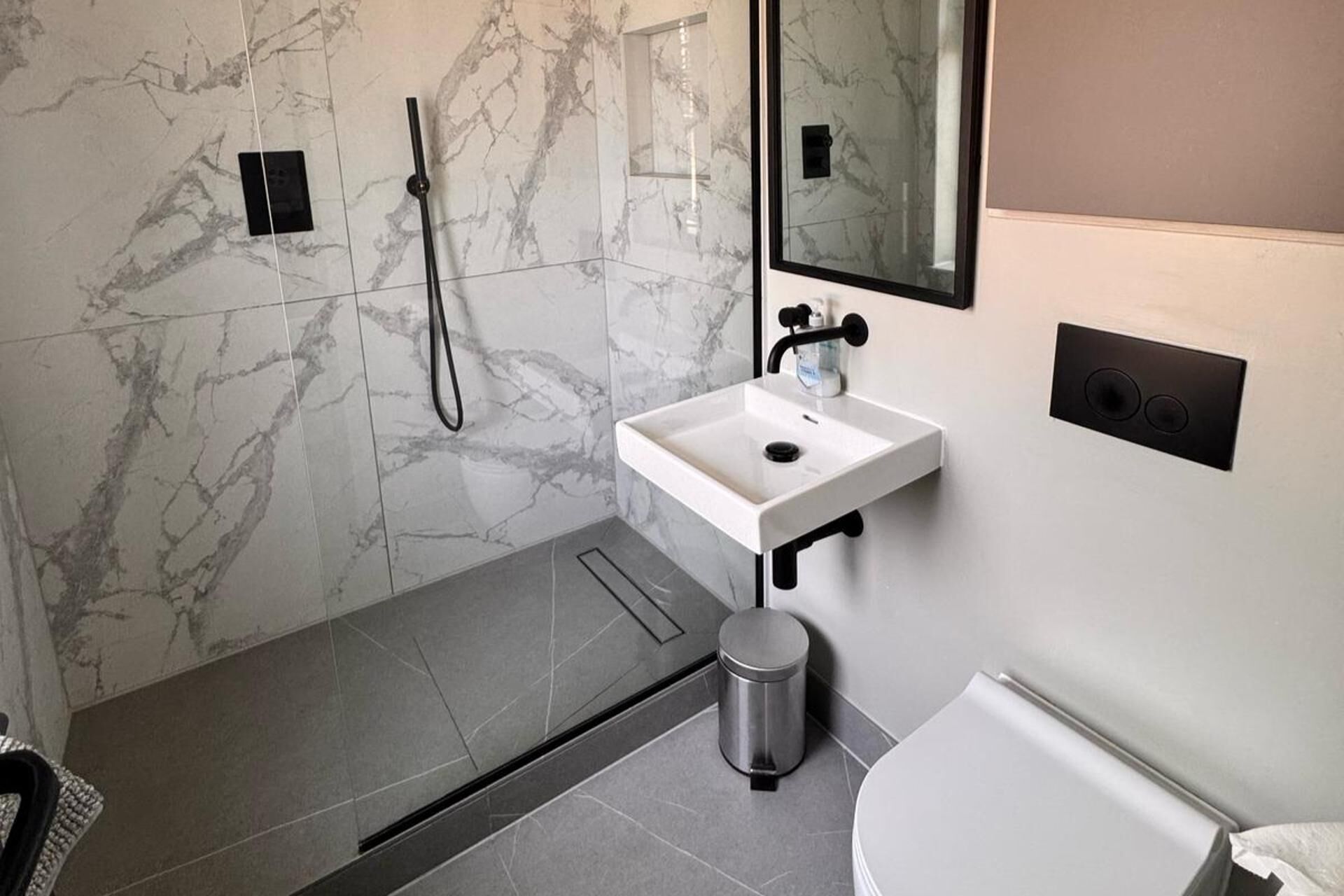 Un bagno moderno con una doccia in marmo, un lavandino bianco e un water.