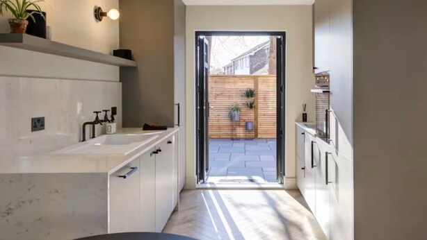 Una cocina moderna con armarios blancos, una isla grande y vistas a una cerca de madera y plantas al exterior.