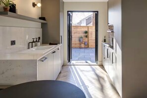 A modern kitchen with white cabinets, a large island, and a view of a wooden fence and plants outside.