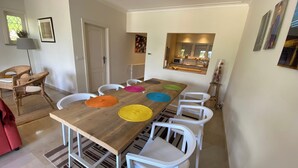 Zona de menjador amb taula de fusta, cadires blanques i sobreades de colors.