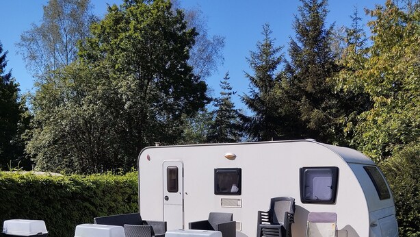 A recreational vehicle with a patio area, including a table and chairs, surrounded by greenery. - Belgian Ardennes lovely 4-person caravan (Saint-Hubert)