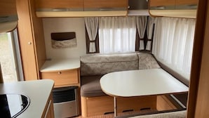 A compact RV interior with a kitchenette, a dining area, and a seating space with curtains. - Belgian Ardennes lovely 4-person caravan (Saint-Hubert)