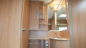 A compact, wooden interior with a sink, mirror, and storage cabinets. - Belgian Ardennes lovely 4-person caravan (Saint-Hubert)