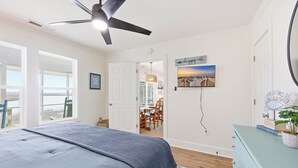 A bedroom with a bed, a ceiling fan, a dining area with chairs and a table, and a dresser with a plant. - Cedar Creek - Creek Front, Mainland, 3-bedroom (Pawleys Island)