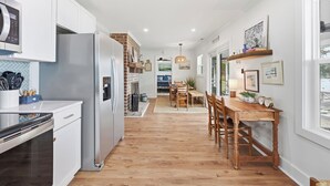 A modern kitchen with white cabinets, stainless steel appliances, and a wooden dining table with chairs. - Cedar Creek - Creek Front, Mainland, 3-bedroom (Pawleys Island)