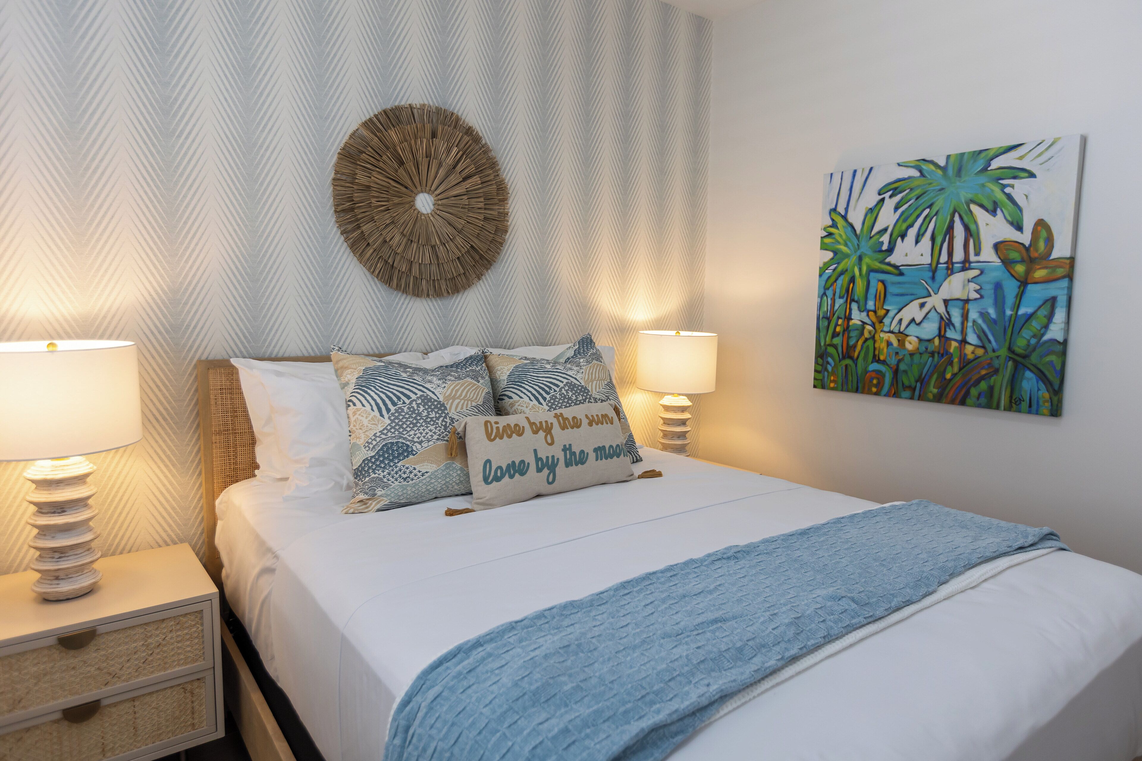 Un lit bien fait, recouvert d’une couverture bleue, avec deux lampes de chevet et un élément décoratif circulaire fixé au mur.