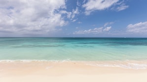 Une plage aux eaux turquoise et limpides, bordée d’un rivage sablonneux, sous un ciel partiellement nuageux.