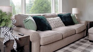 A beige sofa with green and black cushions, a checkered table, and a lamp. - Christmas Tree Farm - Evergreen Escape (Berrien Center)