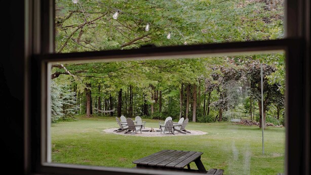A view of a backyard with a fire pit, two Adirondack chairs, and a wooden table. - Christmas Tree Farm - Evergreen Escape (Berrien Center)