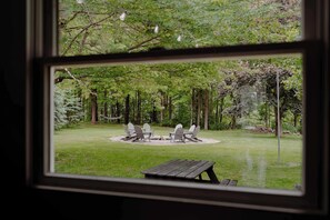 A view of a backyard with a fire pit, two Adirondack chairs, and a wooden table. - Christmas Tree Farm | 16 Acres · Dog-Friendly · Fire Pit (Berrien Center)