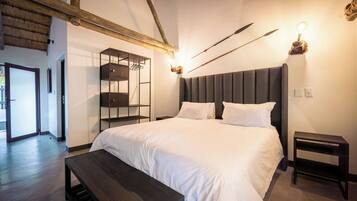 A bedroom with a large bed, a wooden bench, a bedside table, and a wall-mounted shelf.