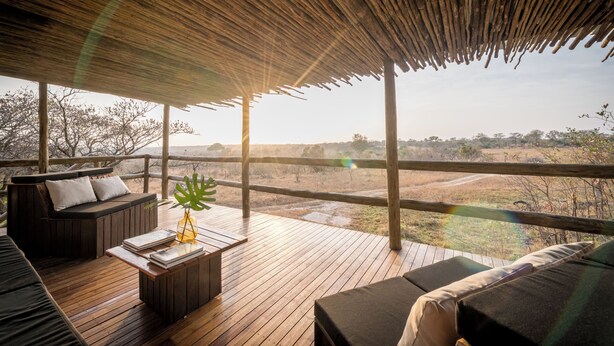 Una terraza de madera con techo de paja, amueblada con un sofá, una mesita de centro y una planta.