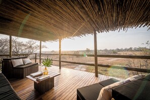 Una terraza de madera con techo de paja, amueblada con un sofá, una mesita de centro y una planta.