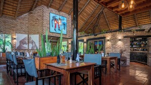 Un restaurante con paredes de ladrillo, mesas y sillas de madera. Hay plantas en macetas y una estatua de ciervo.