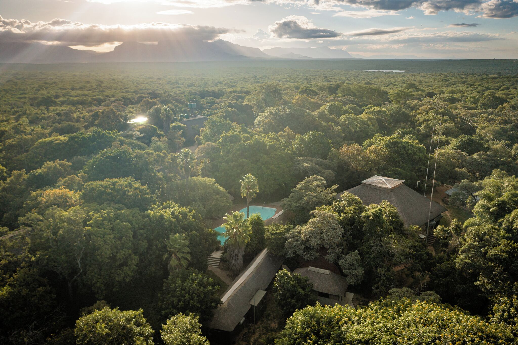 An aerial view of a lush, green landscape with a swimming pool and a building surrounded by dense vegetation.