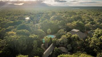 An aerial view of a lush, green landscape with a swimming pool and a building surrounded by dense vegetation.