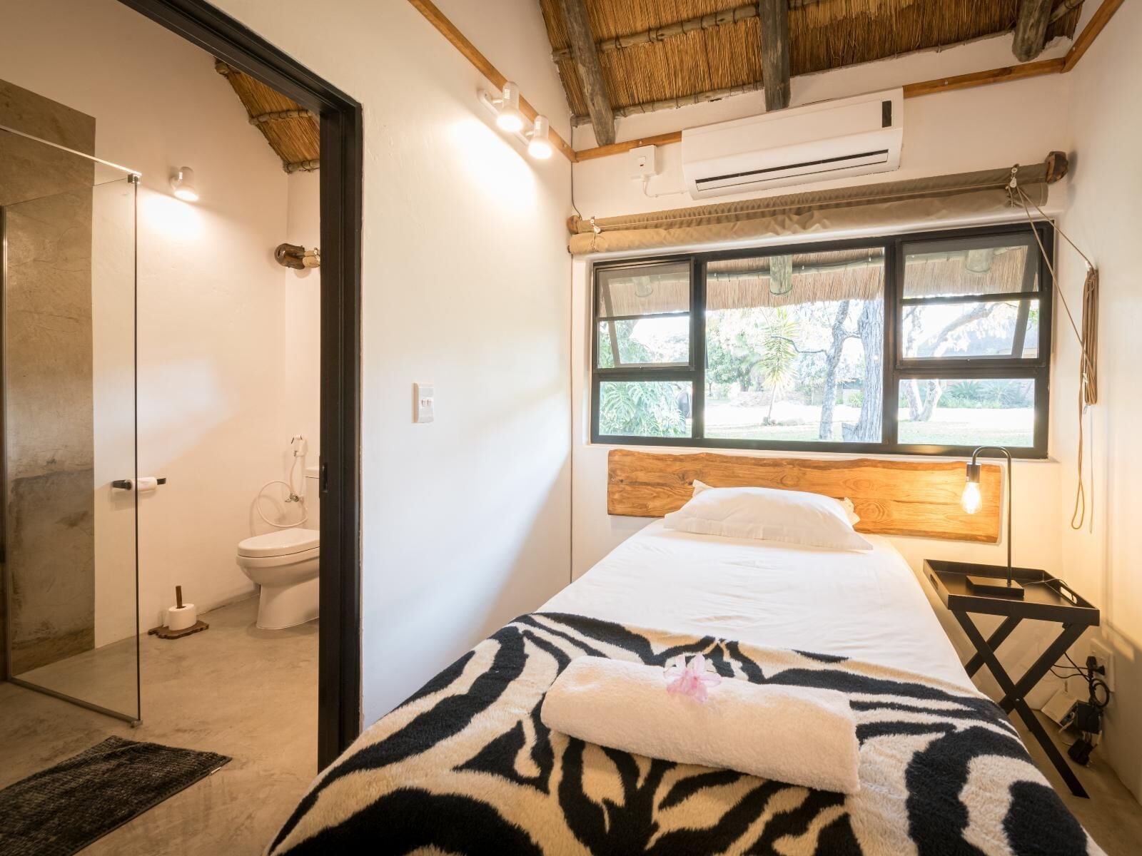 A bedroom with a bed, a window, a wooden headboard, and a nightstand.