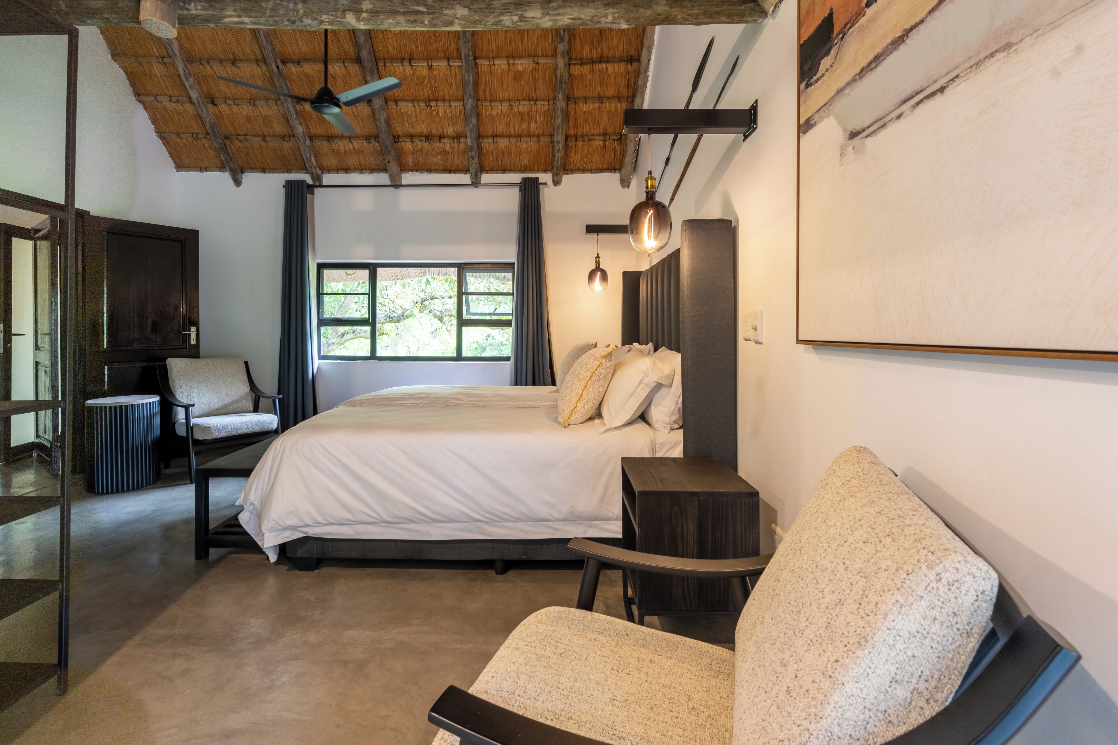 A bedroom with a bed, a chair, a desk, a TV, and a window.