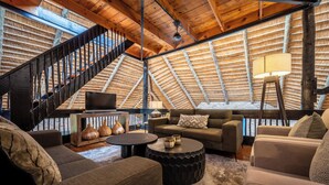 Un acogedor salón tipo loft con una escalera, vigas de madera y un televisor.