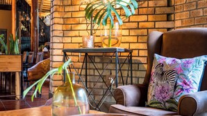 Un rincón acogedor con un muro de ladrillo, un sillón con cojín estampado de cebra y una mesita con un jarrón de cristal.