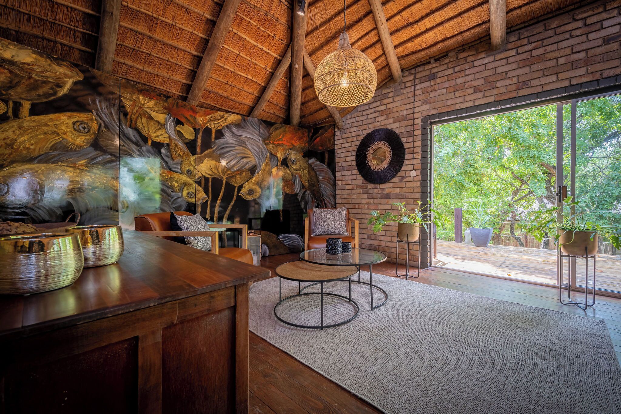 A rustic interior with a wooden ceiling, a round table, and a large window overlooking greenery.