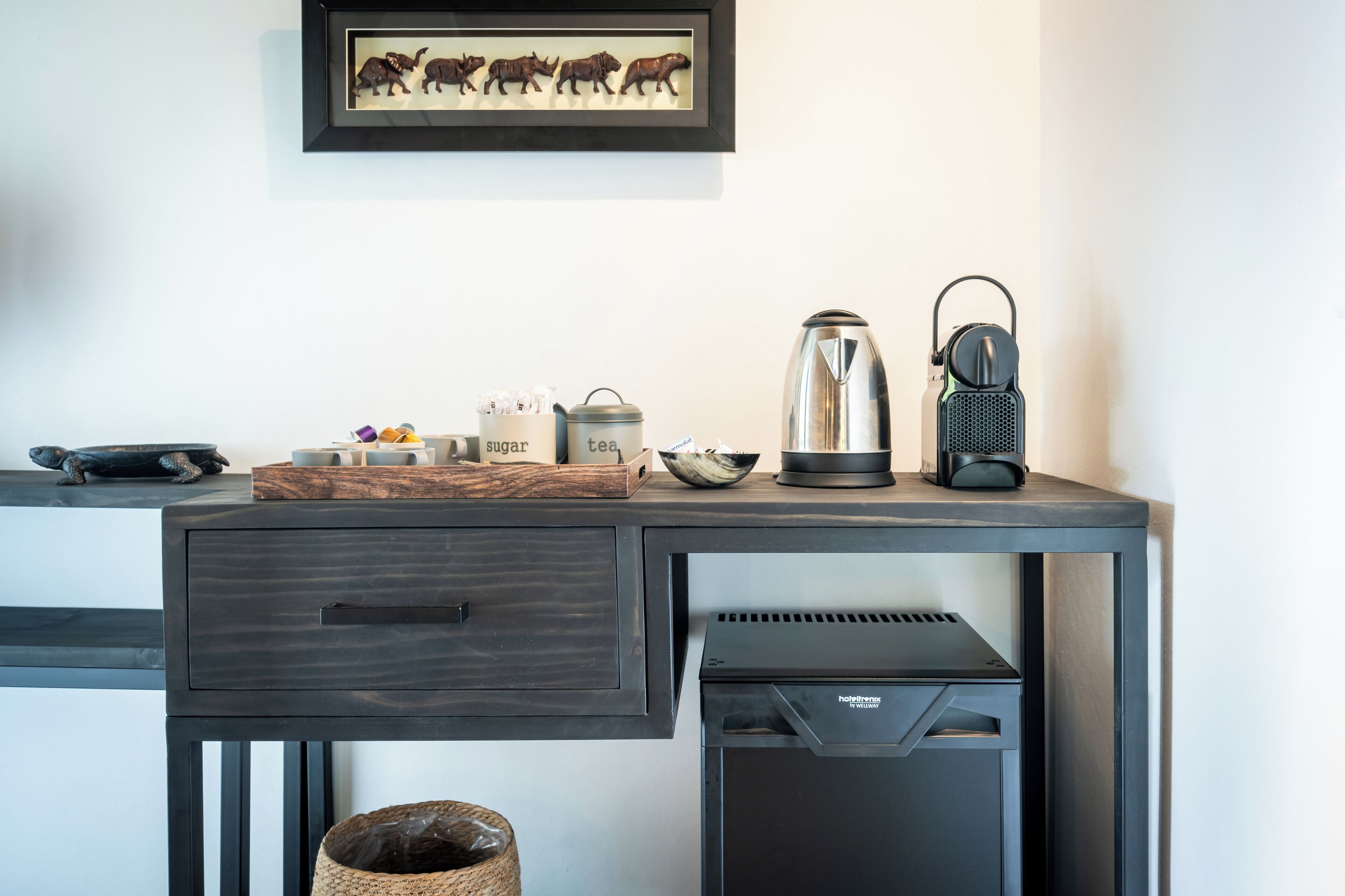 A modern kitchenette with a coffee maker, tea pot, and sugar and tea containers on the counter.