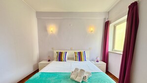 Een hotelkamer met een bed, twee nachtkastjes, een raam met gordijnen en wandlampen.