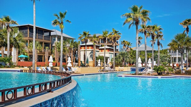 Un resort con una amplia piscina, palmeras y varios edificios con balcones.