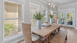 Comedor con mesa de madera, sillas de mimbre, plantas en macetas y una lámpara moderna.