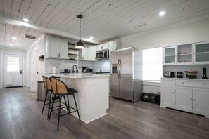 Een moderne keuken met witte kastjes, een roestvrijstalen koelkast en een centraal kookeiland met barkrukken.