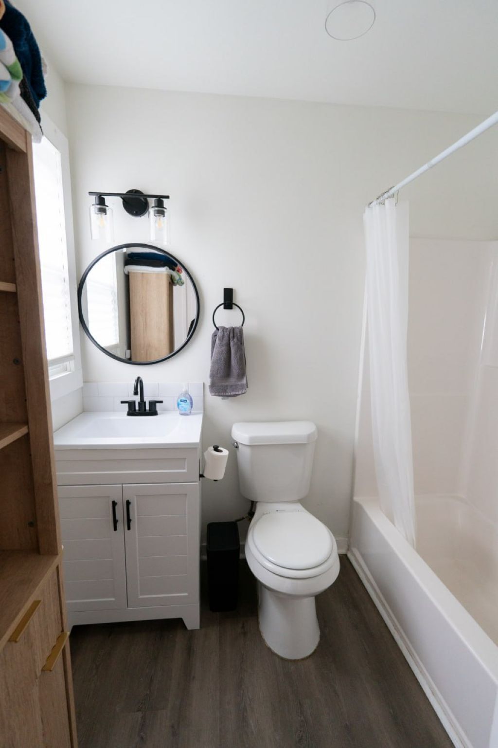 Een badkamer met een witte wastafel, een ronde spiegel, een toilet en een douchegordijn.