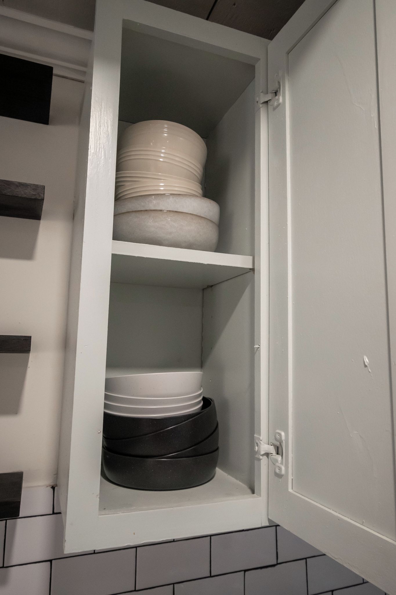 A cabinet with multiple shelves containing white and black plates.