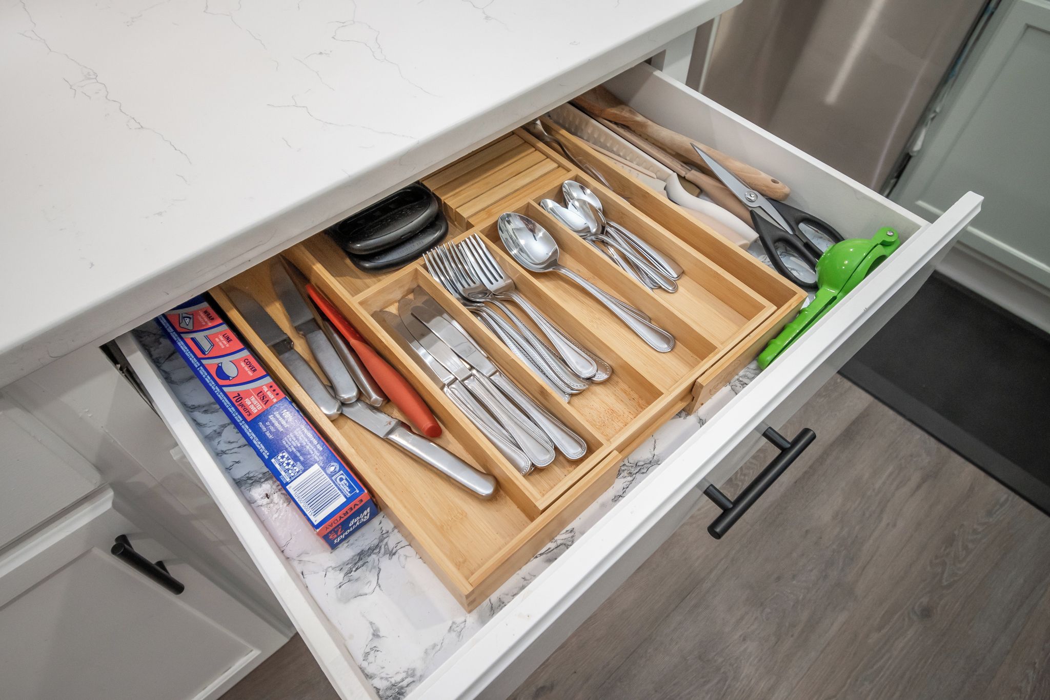 Un cajón de cocina con utensilios y una caja de azulejos.