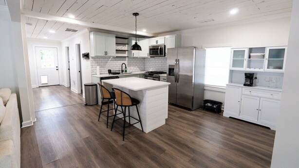 Een moderne keuken met witte kasten, een roestvrijstalen koelkast en een centraal eiland met barkrukken.