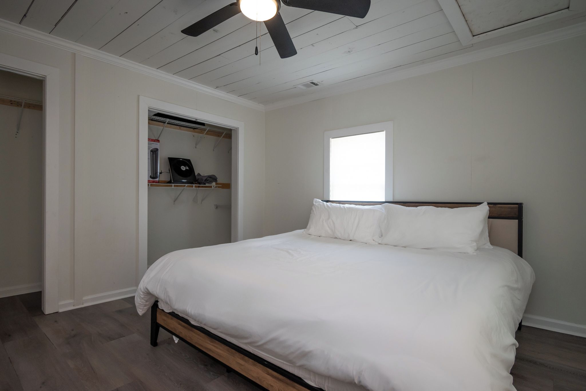 A bedroom with a bed, a ceiling fan, a window, and a walk-in closet.