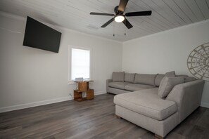Een moderne woonkamer met een hoekbank, een plafondventilator, een flatscreen televisie en een decoratief wandobject.