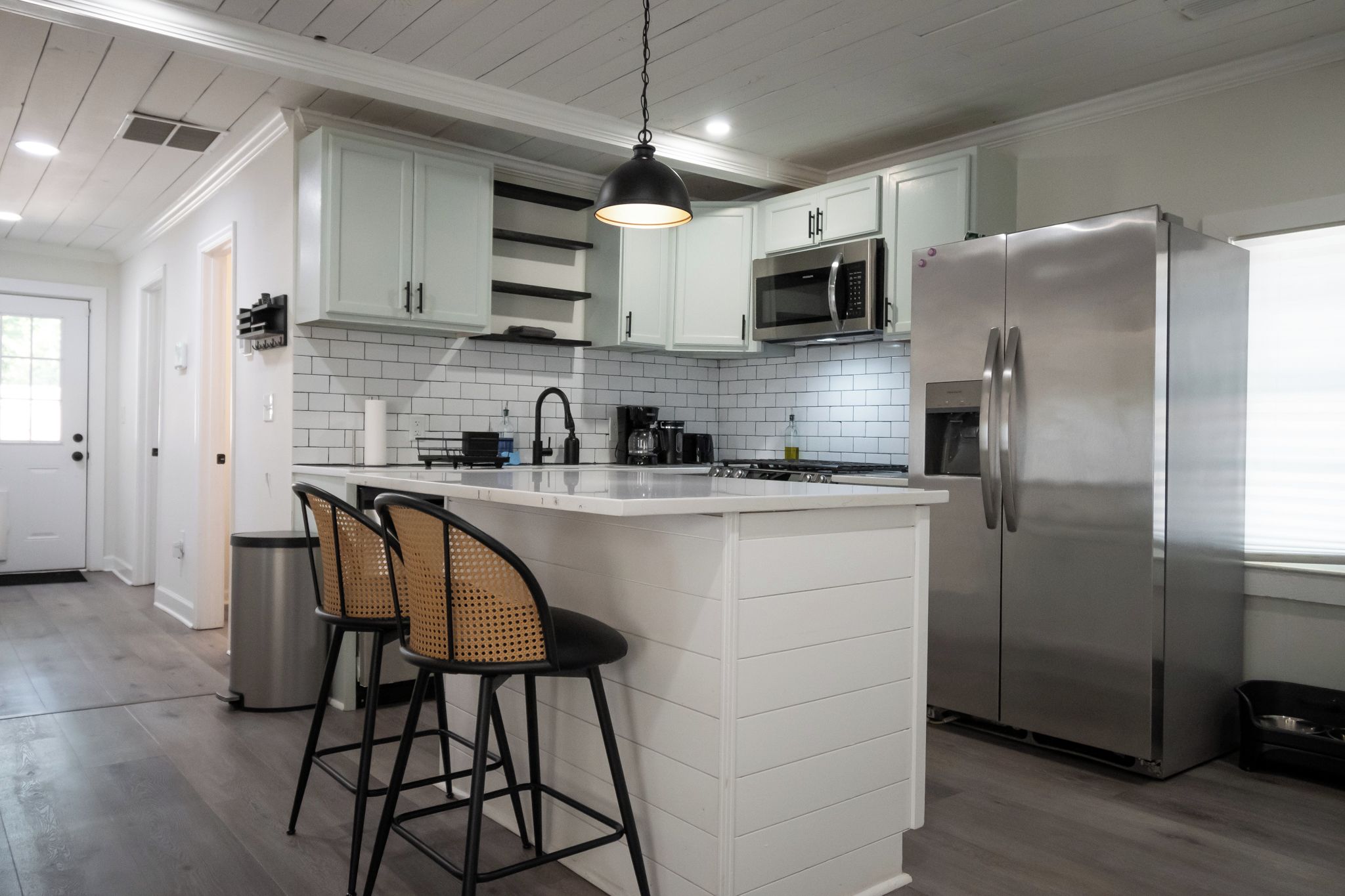 A modern kitchen with white cabinetry, a stainless steel refrigerator, a microwave, and a hanging pendant light.