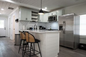 A modern kitchen with white cabinetry, a stainless steel refrigerator, a microwave, and a hanging pendant light.