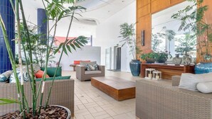 A spacious lobby with wicker furniture, large potted plants, and a wooden reception desk. - Apto pé na areia na Riviera São Lourenço (Bertioga)