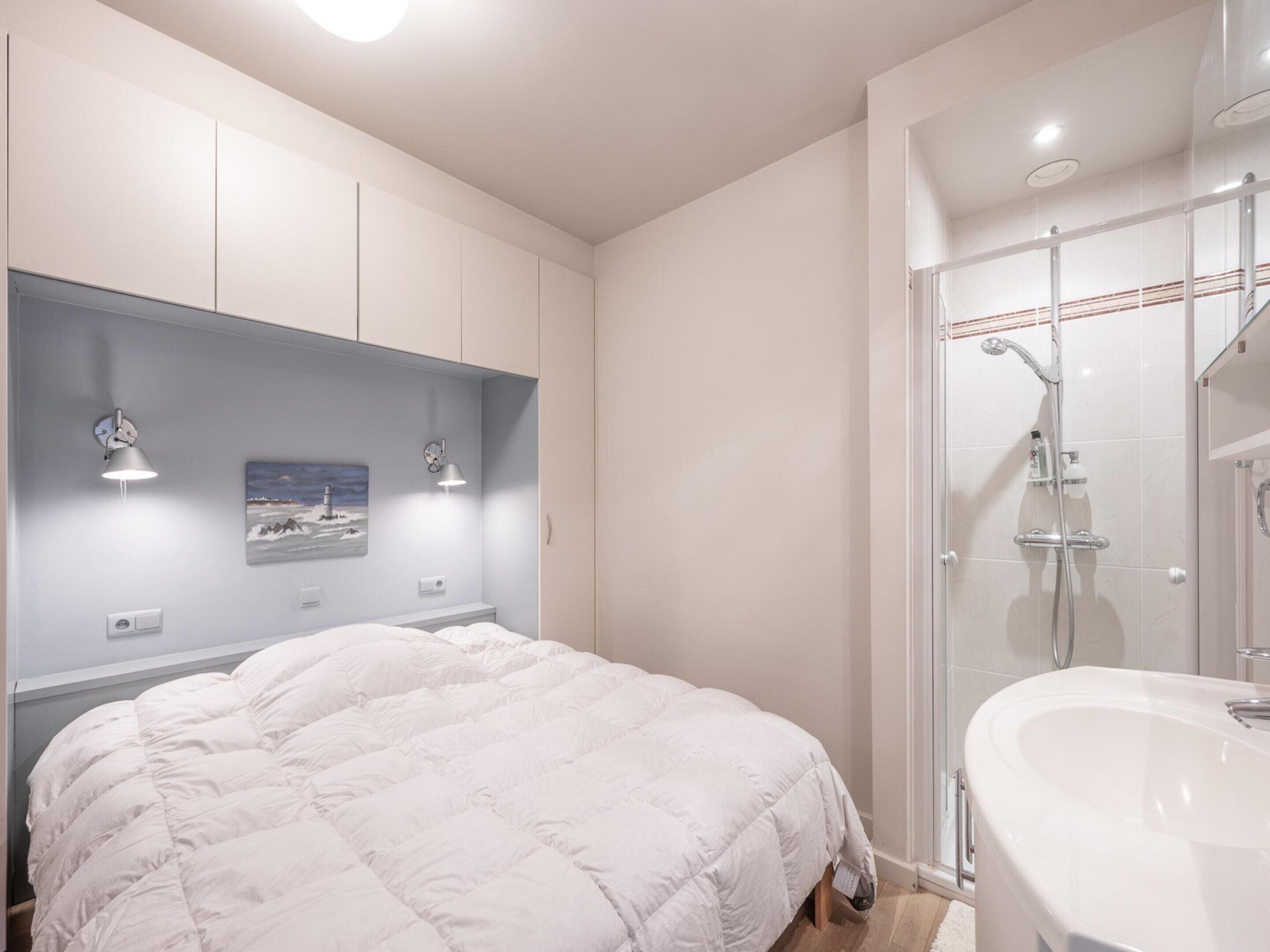A bedroom with a bed, a nightstand, a wall-mounted lamp, and a picture.