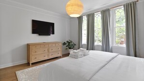 Un dormitorio con cama, cómoda, televisor y ventana con cortinas.