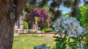 Un jardín cuidado con una mecedora, un árbol y un edificio al fondo.