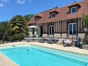 Una casa de dos pisos con piscina, mobiliario exterior y jardín.