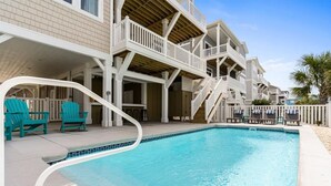 Une piscine dotée d’une terrasse blanche, de chaises turquoise et d’une zone de pont en bois.