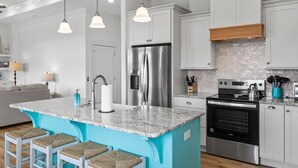 Une cuisine moderne dotée d’un îlot central, d’appareils électroménagers en acier inoxydable et de luminaires suspendus.
