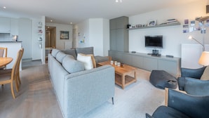 A modern living room with a grey sofa, a wooden coffee table, and a TV mounted on the wall. - Apartment in Knokke Near the Beach (Knokke-Heist)