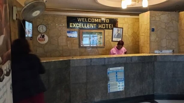 Un comptoir d’accueil avec une pancarte indiquant « Bienvenue à l’hôtel Excellent », une horloge et un tableau encadré accroché au mur.